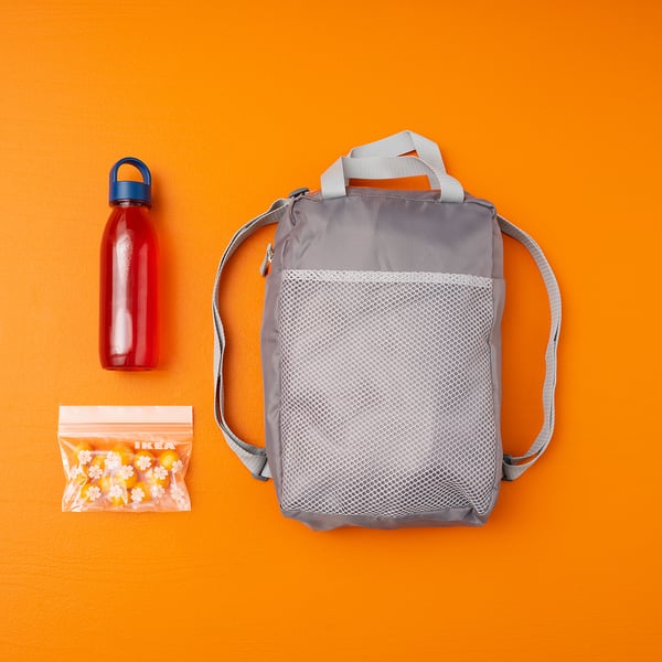Grey polyester backpack with bottle & snacks in mesh pocket, orange backdrop.