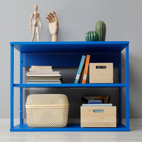 Blue metal shelving unit with books, decorative items, and storage bins. Top holds a wooden figure and cactus.