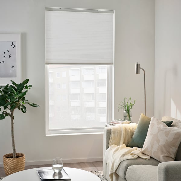 Modern living room with PRAKTLYSING white blinds, sofa, pillows, rug and plant.