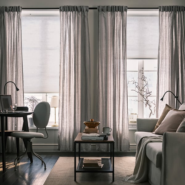 Modern living room with large window, curtains, desk, sofa, books, coffee, and lamp.