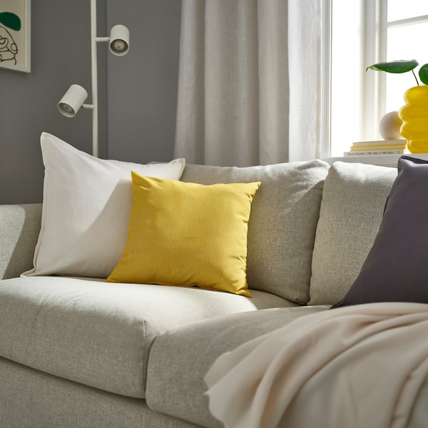 Yellow PROFETBLOMMA square cushion on grey sofa, with subtle pattern, other cushions, beige blanket.