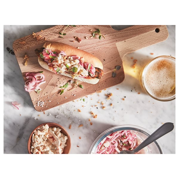 A gourmet sandwich with beer and condiments on a cutting board.