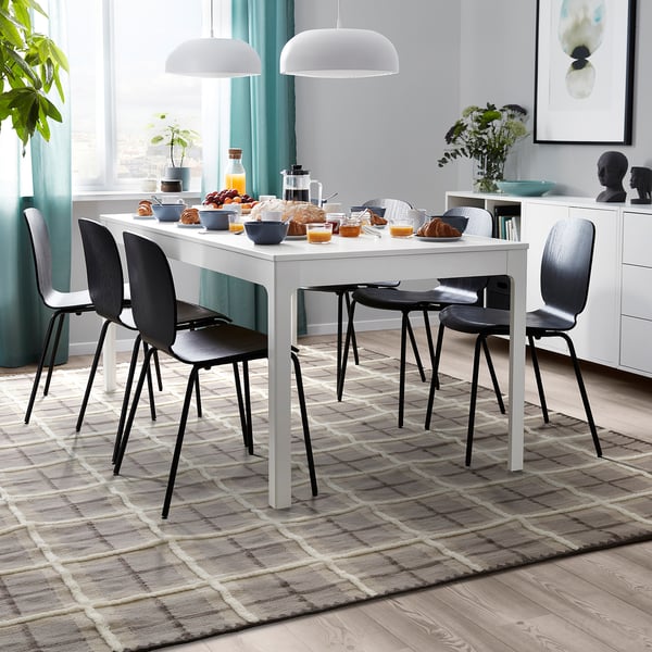 Modern dining room with brown/grey tartan wool rug, white table & black chairs, teal curtains, & decorative items.