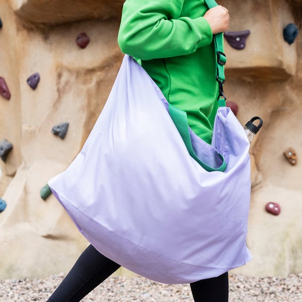 Person wearing bright green top holding large light grey RÄCKLA bag made of recycled polyester, suitable as extra travel bag.