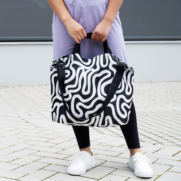 Person holding RÄCKLA bag, black & white swirl design, small to medium size, easy to carry.