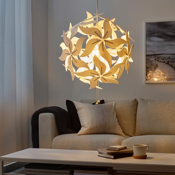 Unique RAMSELE pendant lamp, beige, textile leaves design. Hangs above a modern beige sofa with cushions. Soft lighting, decorative ceiling patterns.