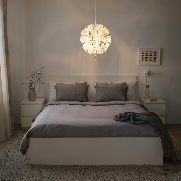 Modern bedroom with large RAMSELE pendant lamp over king-sized bed, grey bedding, nightstands with vases.