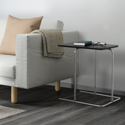 Small side table next to a grey sofa. Table holds a book and glasses, useful for reading or relaxing.