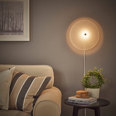 Round wall lamp on grey wall beside photo, above a striped-cushion sofa and round table with books, box, and plant.