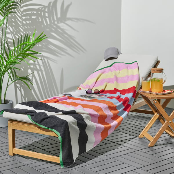 Colourful striped ROSENOXALIS towel on a deck lounge. Bright colours, large size, cotton/viscose blend, with wooden side table and drink.