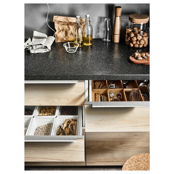 Modern kitchen countertop with wooden drawers and various items including bottles, jars, and woodchips.