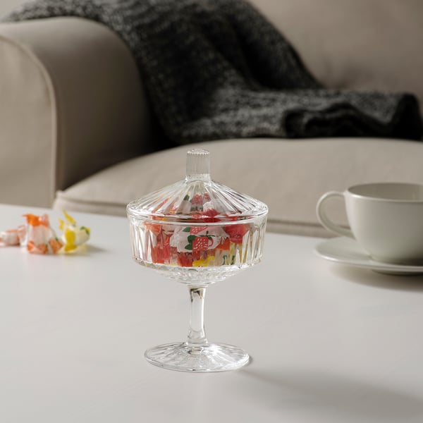 Clear glass candy jar with lid on table, next to tea cup and sofa. Holds 0. 2 litres.