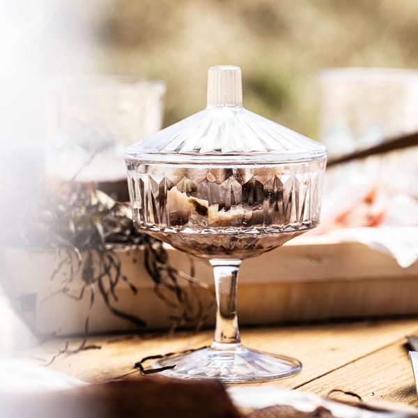 Clear glass candy jar with lid on wooden table. Decorative diamond pattern, versatile use.