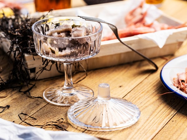 Glass bowl with lid, holding tuna sashimi, on rustic wooden table.