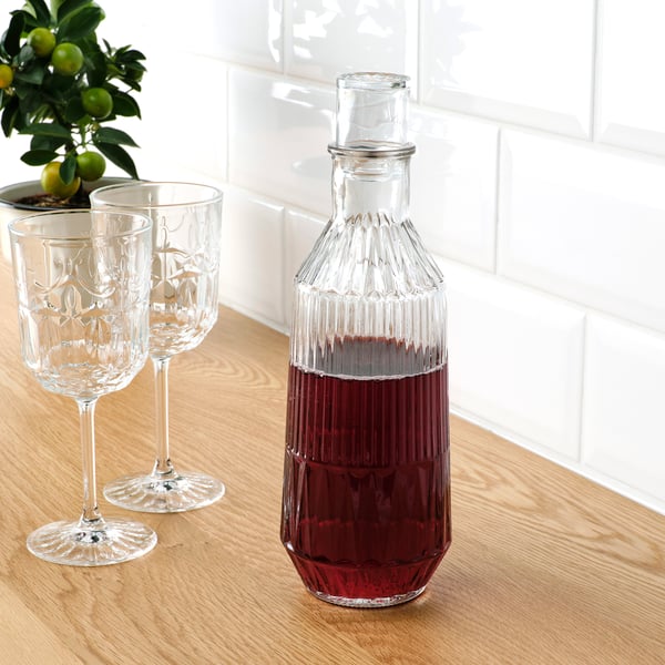 Clear glass decanter with red liquid and two matching glasses on wooden counter.