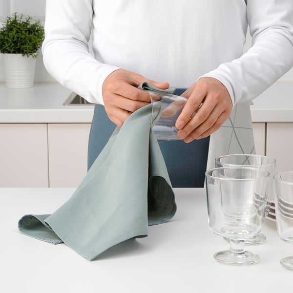 Person folding light blue kitchen towel near glasses.