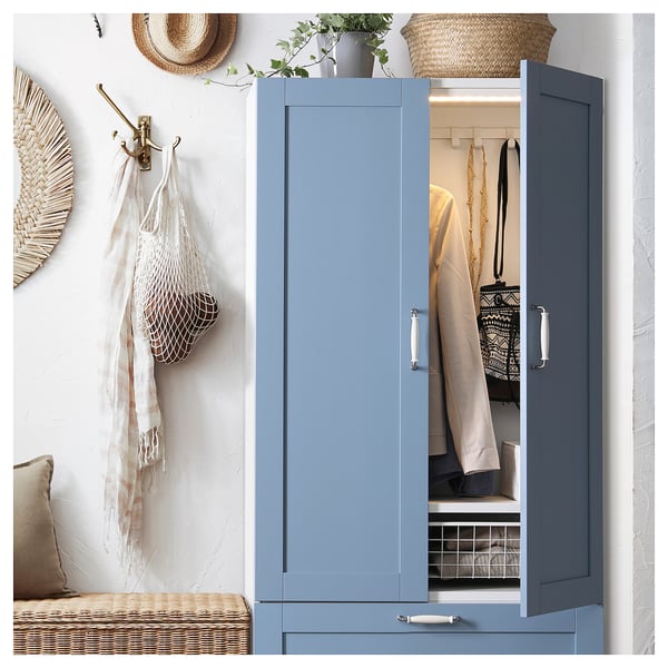 Blue SANNIDAL closet with clothes, handles, and decorative items against a white wall.