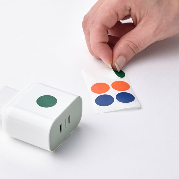 Hand placing sticker on usb-c charger. Charger has green sticker, suitable for multiple devices.