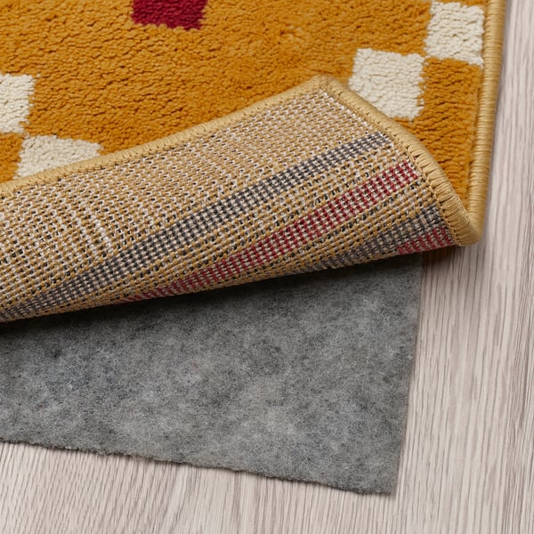 Yellow patterned rug with non-slip lining on top of felt mat.