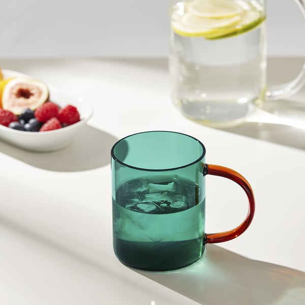 Teal iced mug with orange handle on bright table by fruit.