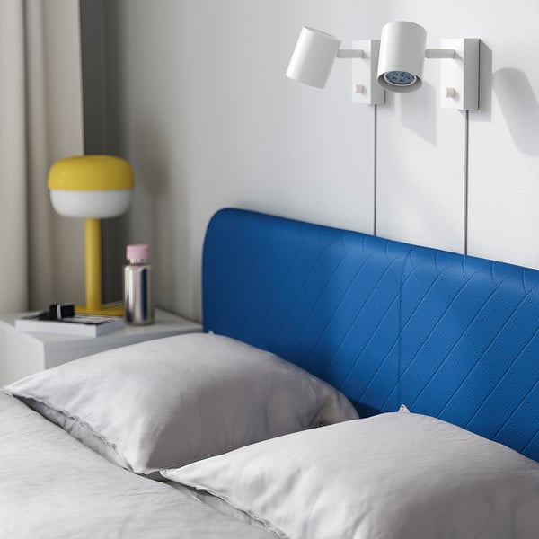 Bedroom scene featuring blue SLATTUM bed frame with white linens, yellow lamp, and wall-mounted lights.