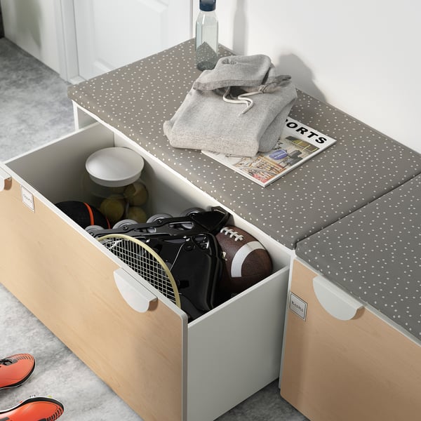 Open storage bench, beige and grey, wood-like panels, white sports equipment inside, grey sweatshirt on top.