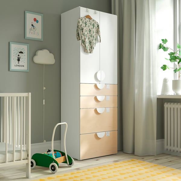 Modern baby nursery with SMÅSTAD wardrobe in white and wood tones, green toy car, hanging onesie, and framed art.
