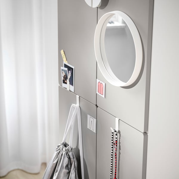 A modern, grey SMÅSTAD wardrobe with a round mirror and hooks. It has multiple compartments and holders displaying items like pictures and bags.