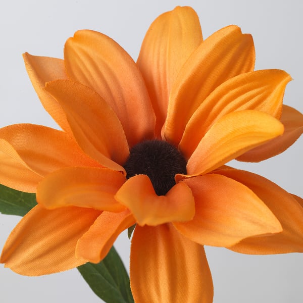 Orange artificial daisy with green leaves, recycled, vibrant petals and black centre, plain background.