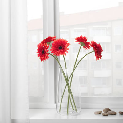Vase with three red artificial flowers near a window.