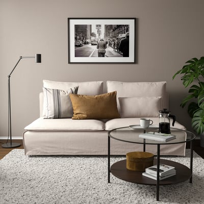 Modern living room with beige SÖDERHAMN sofa, cushions, black lamp, glass coffee table, and green plant.