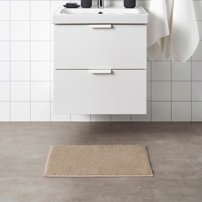 Beige SÖDERSJÖN bath mat next to sink. Rectangular, cotton, latex-backed.
