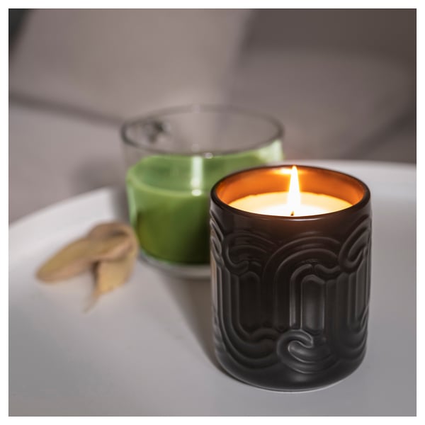 Two lit candles on a table: one green, one black with glowing flame, emitting a fresh scent of green matcha, ginger, and citrus.
