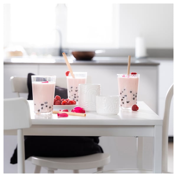 Pink bubble tea drinks with straws on white table, surrounded by berries, minimalist setting.