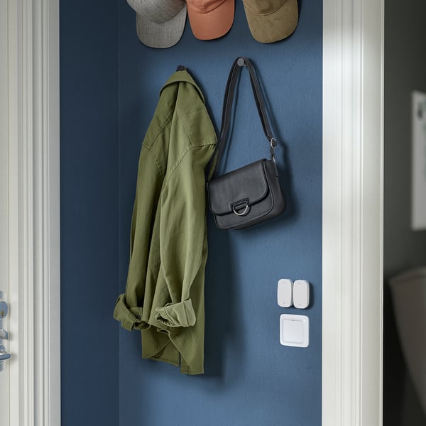 A blue wall, mounted with a jackets, hats, and a handbag. Below, a button for smart home automation.