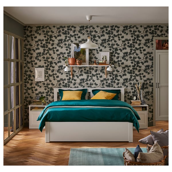Modern bedroom with a white SONGESAND bed, teal bedding, wooden floors, floral wallpaper, and yellow pillows.