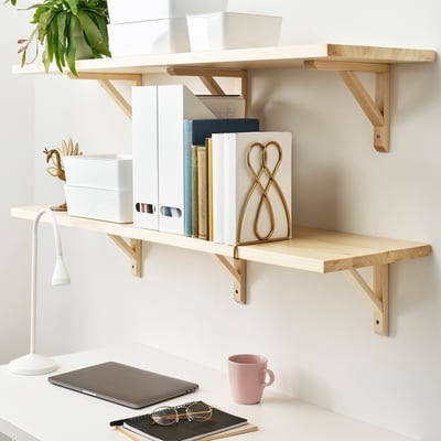 Desk with shelves holding books, storage boxes, a lamp, a mug, and a plant. Books are kept in place by a slidable bookend.