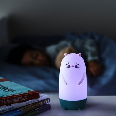Cat-shaped night light on stack of books, emitting soft glow. Ideal for kids rooms, offering seven colour changes.