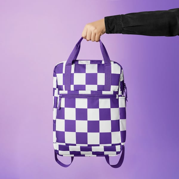 Person holding a purple and white chequered backpack against a purple background. The backpack adjustable straps and multiple compartments.