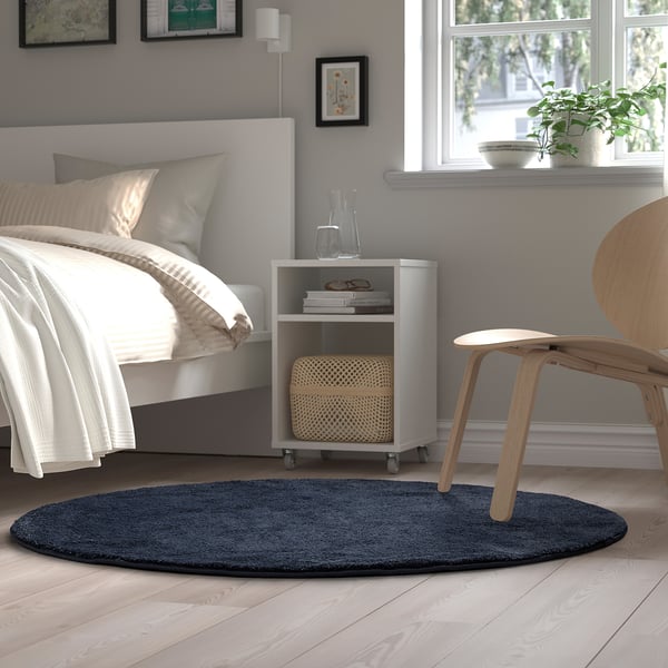 Cosy bedroom with blue rug, wood floors, bed, bedside table, plants, chair.
