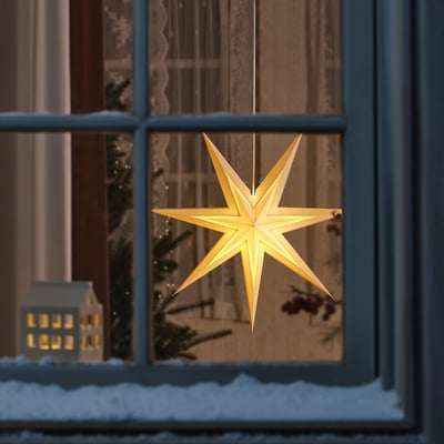 A warm, illuminated star decoration hangs near a window, casting a cosy glow, alongside a small lit house model and festive holiday greenery.