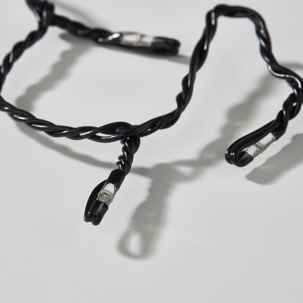 Black twisted led light chain with small diodes, laying slightly tangled, casting shadows.