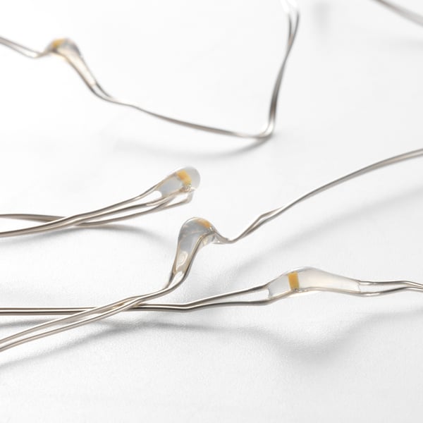 Close-up of delicate white string lights with small, warm glowing bulbs. Wires gently curve, showcasing quality design and craftsmanship.