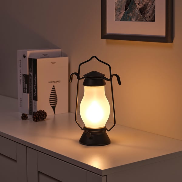 Vintage lantern lamp on table with books and pine cone, emitting warm light.