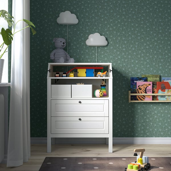 Childs room with white SUNDVIK dresser, bear mobile, toys, books, and patterned wallpaper. Dresser is moderate in size compared to other items.