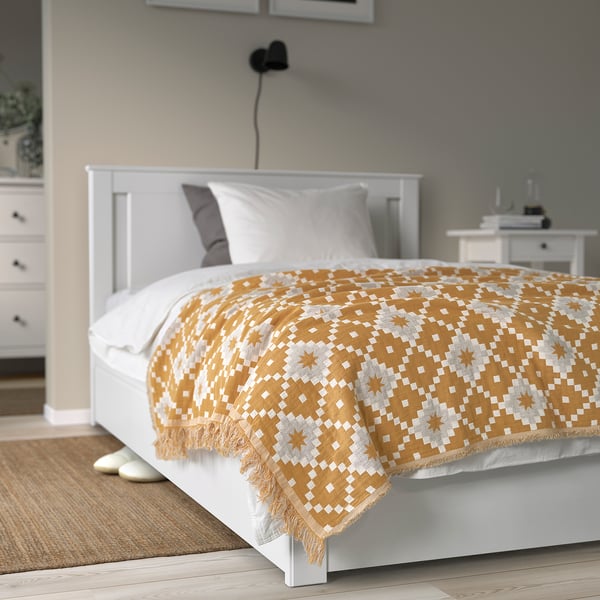 Bed with SVARTFRYLE throw in yellow/grey, neat with bedside table, cosy atmosphere.