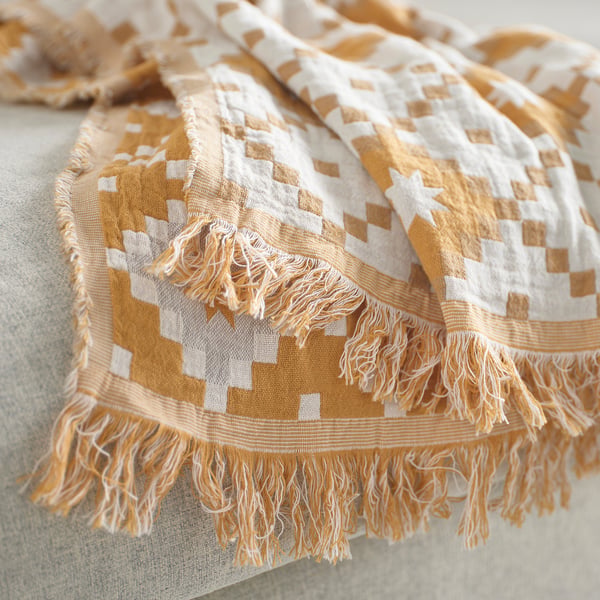Folded, woven throw with yellow and white pattern; fringe detail.