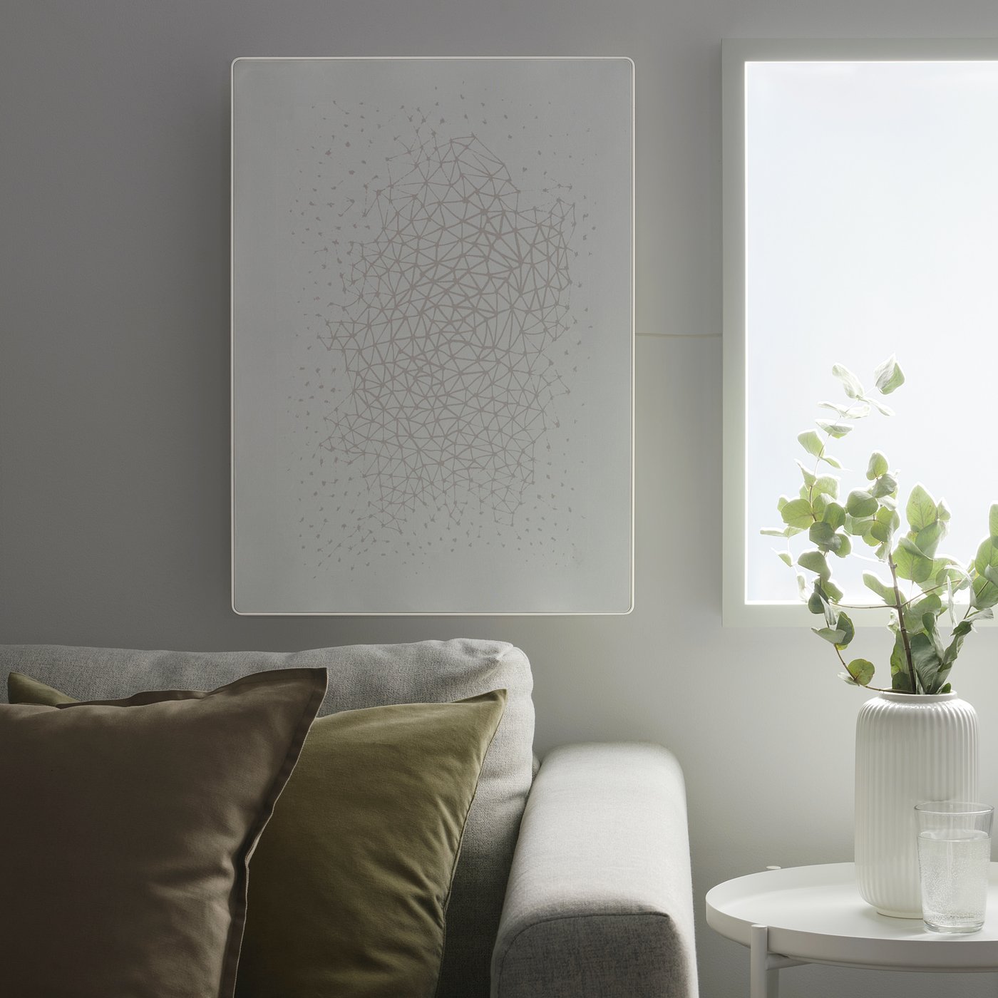A symfonic wifi speaker-picture frame above sofa, side table with vase, glasses.