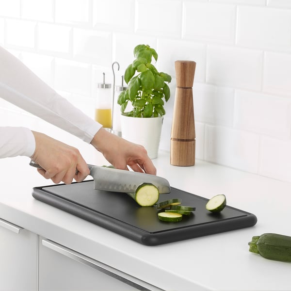 Person chops courgette on durable black cutting board with grooves that collect juice; gentle on knives.