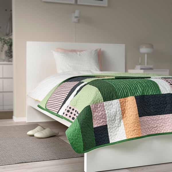 Colourful patchwork bedspread on large bed with recycled polyester, striped pillow, slippers.